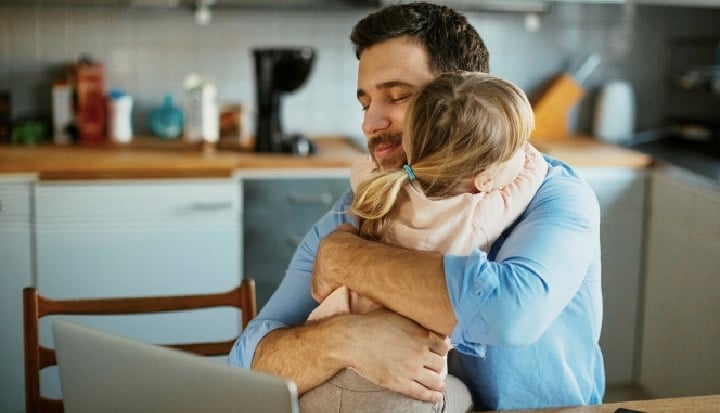 Parents in the Workplace: Father working from home hugging daughter