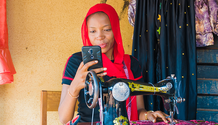young women at sewing machine looking at her phone