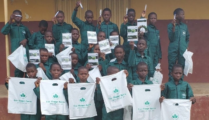 Group of school children in Nigeria dressed in a green uniform and holding white bags