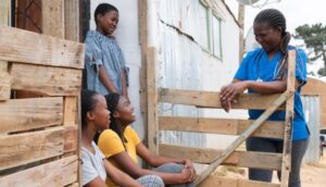 Delivering Healthier Futures for Women, Children and Young People: community-nurse-talking-happliy-to-teenage-girls-in-an-informal- settlement